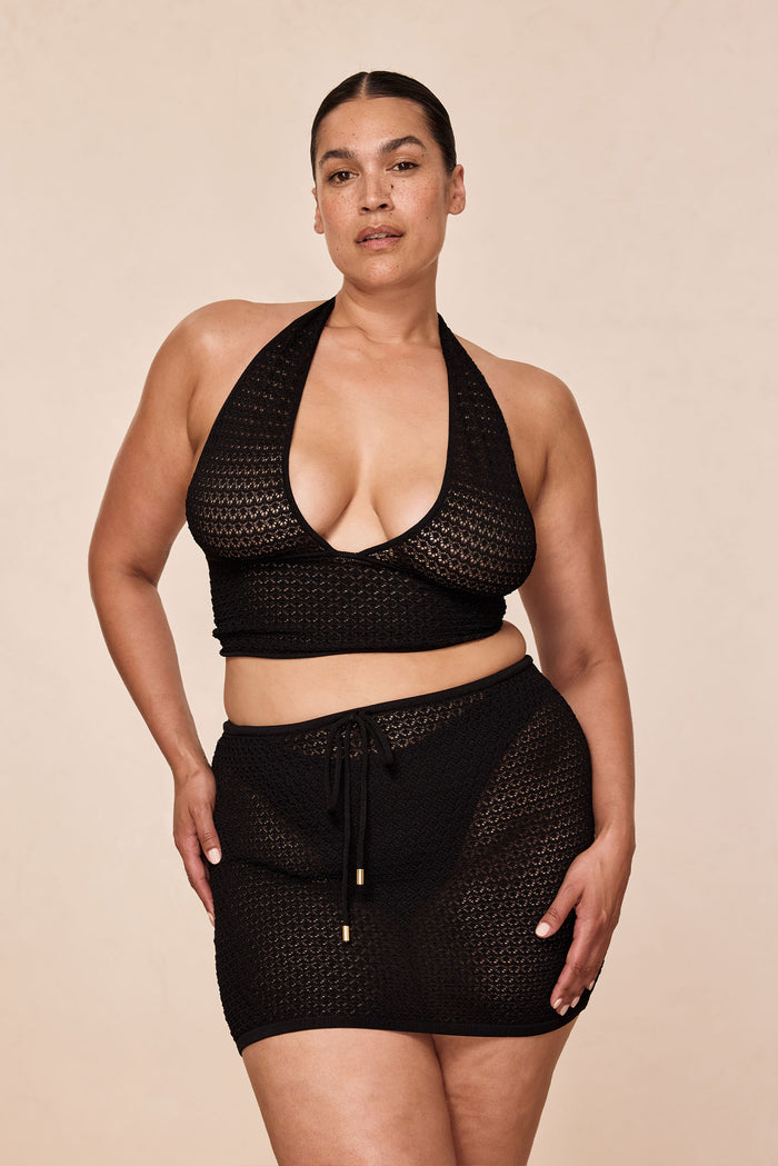 Front view of Toulon Top in Black Lace Crochet on model showing deep V halter neckline and banded waist, beige background