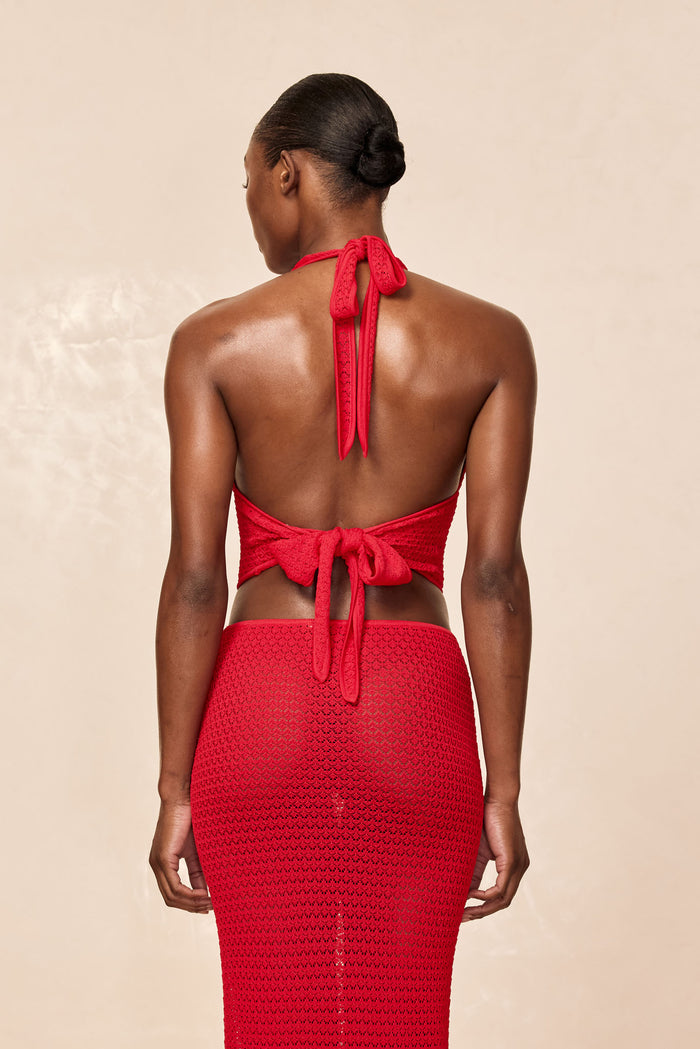 Back view of a model wearing a red crochet halter tie top with back bow and a matching fitted crochet skirt.