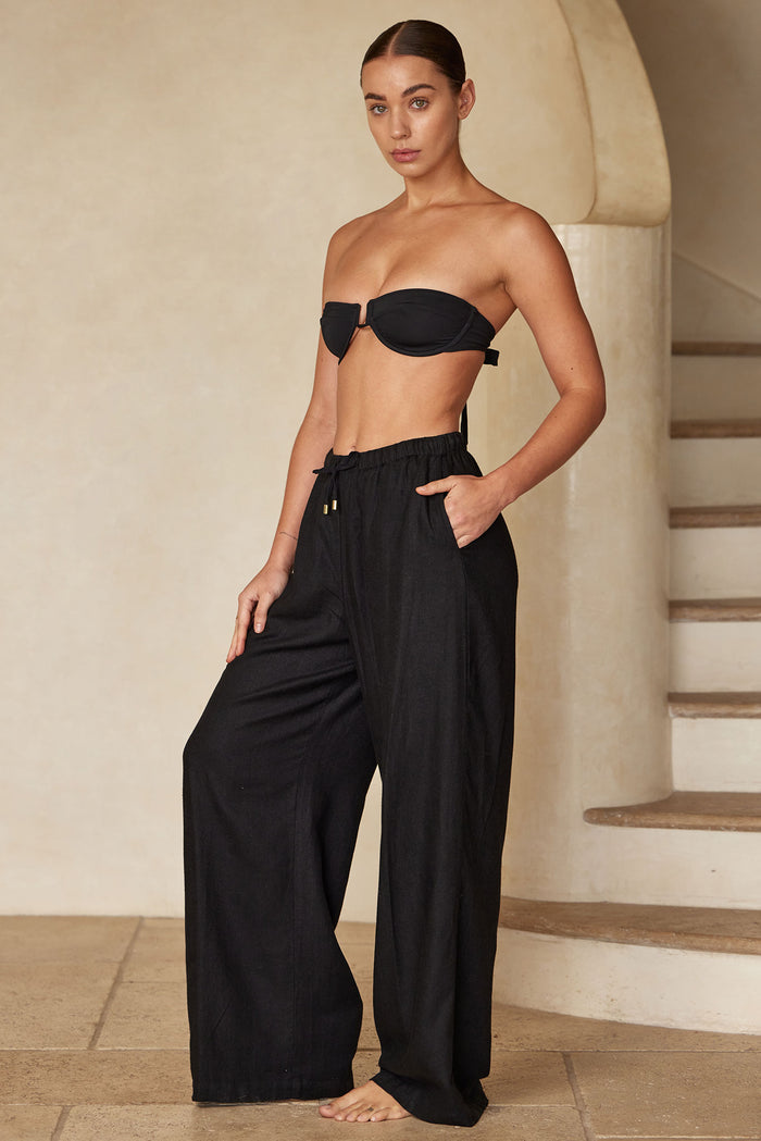 Front view of Tuscany Pant in black showing wide-leg silhouette and elastic drawstring waist on model by curved staircase