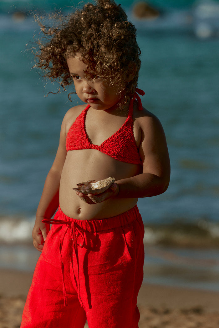 Front view of Tuscany Pant Kids in Chili Pepper showing elastic drawstring waistband and relaxed relaxed fit on a child at the beach