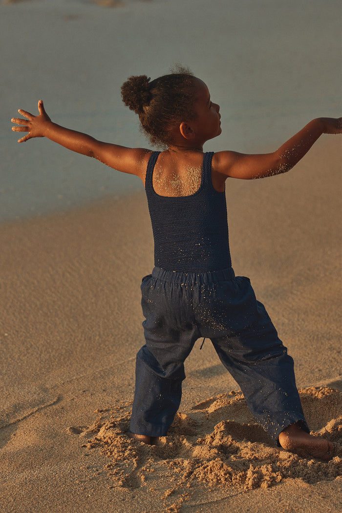 Rear view of Tuscany Pant Kids - Midnight showcasing smocked waistband and relaxed flare leg on a child at the beach