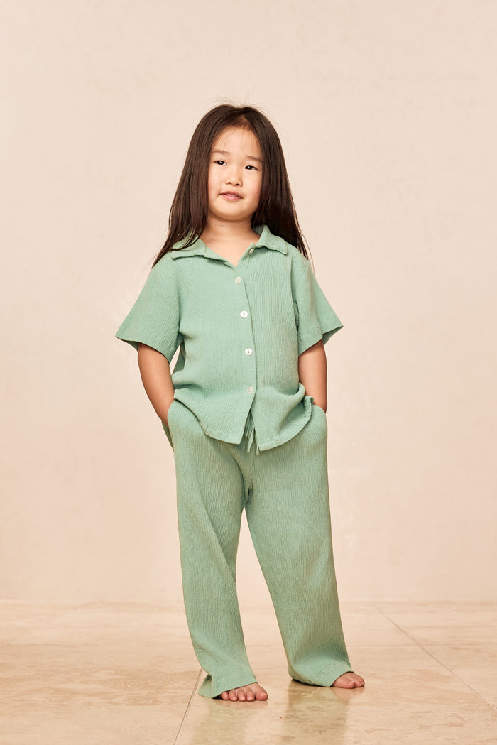 Front view of Tuscany Pant Kids in Pond Crinkle showing smocked waistband and relaxed flare leg on child model against a neutral beige background
