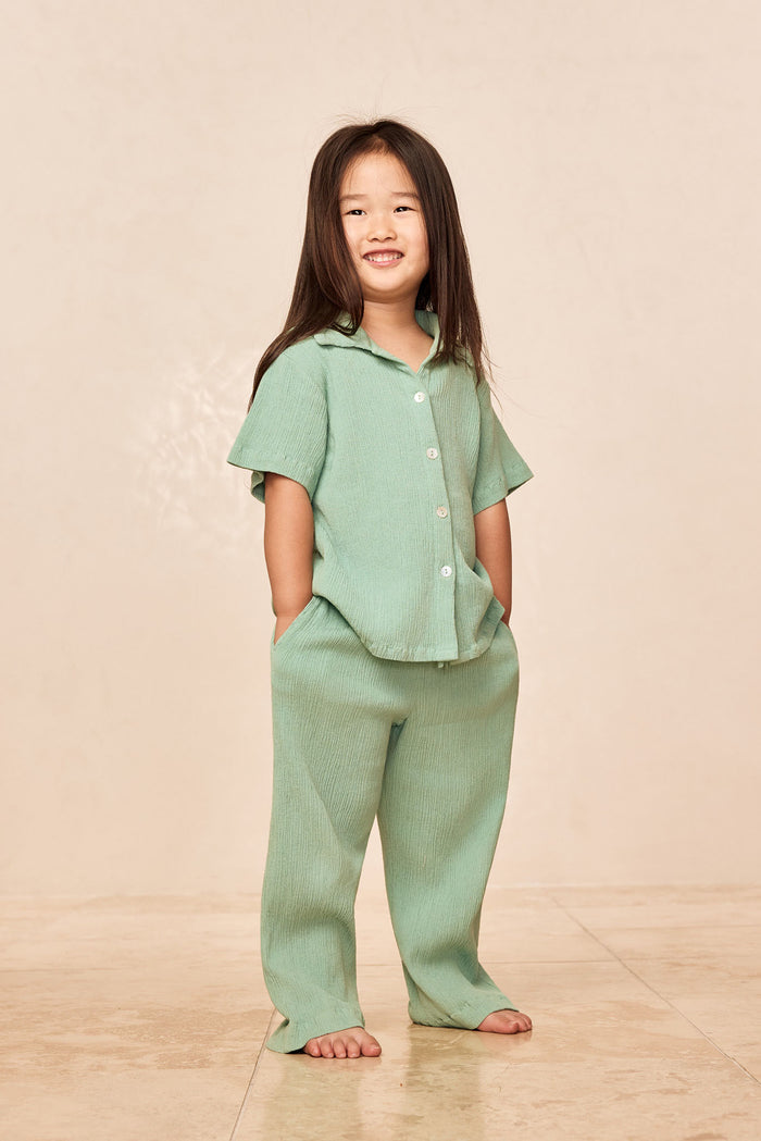 Three-quarter front of Tuscany Pant Kids in Pond Crinkle showing crinkle texture, smocked waistband and relaxed flare on a child