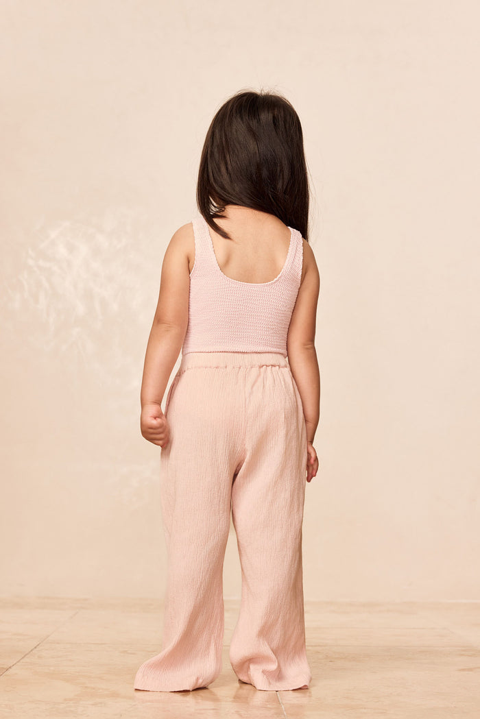 Back view of Tuscany Pant Kids in Powder Pink Crinkle showing smocked waistband and crinkle fabric on child, beige background
