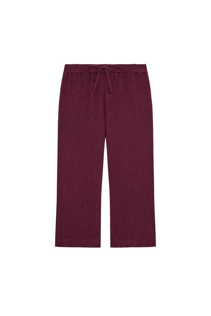 Front flat lay of Tuscany Pants Kids in fig showing smocked waistband, drawstring, crinkle texture and flare leg on white