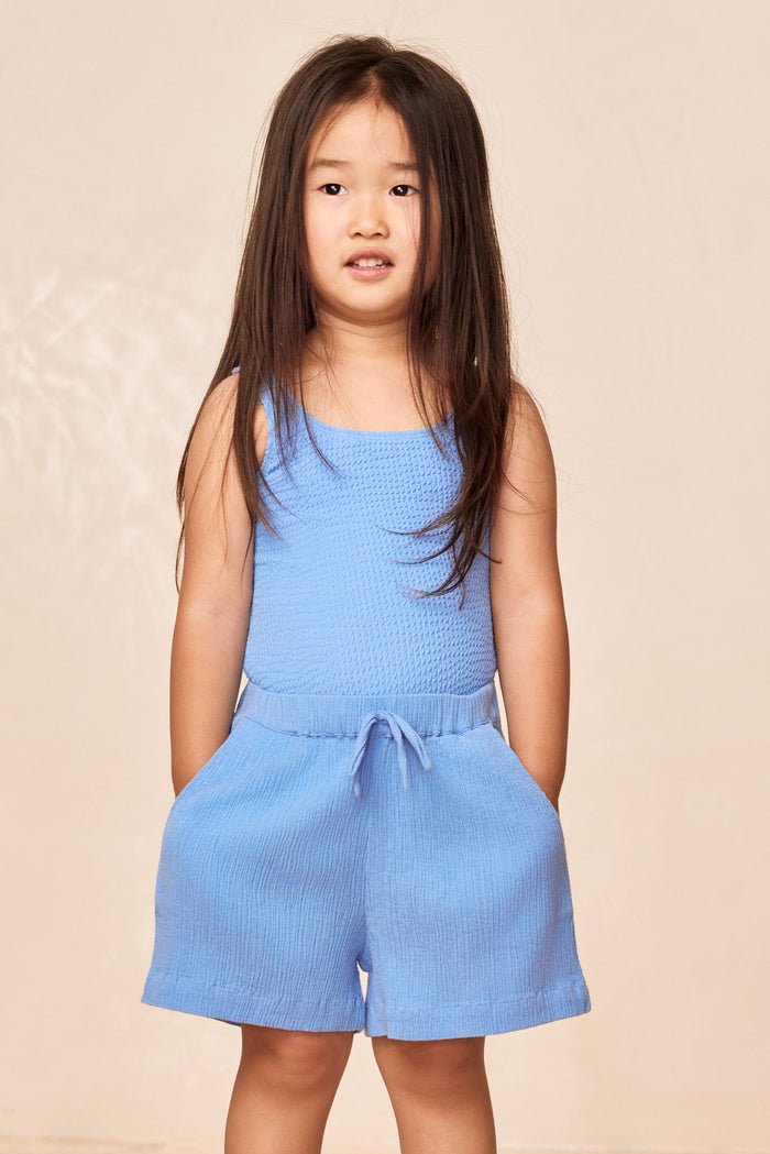 Front view of Tuscany Short Kids shorts in Azure Crinkle, crinkle texture, drawstring waist and pockets on beige backdrop