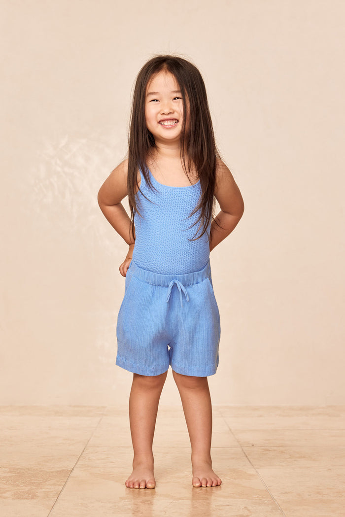 Front view of Azure Crinkle kids shorts on model, showing crinkle texture and elastic waist with faux tie on beige background
