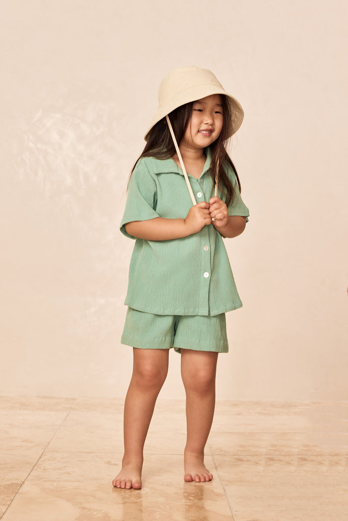 Front view of Tuscany Short Kids in Pond Crinkle showing crinkled fabric, elastic waist, and pull-on shorts worn by a child model on a beige studio background