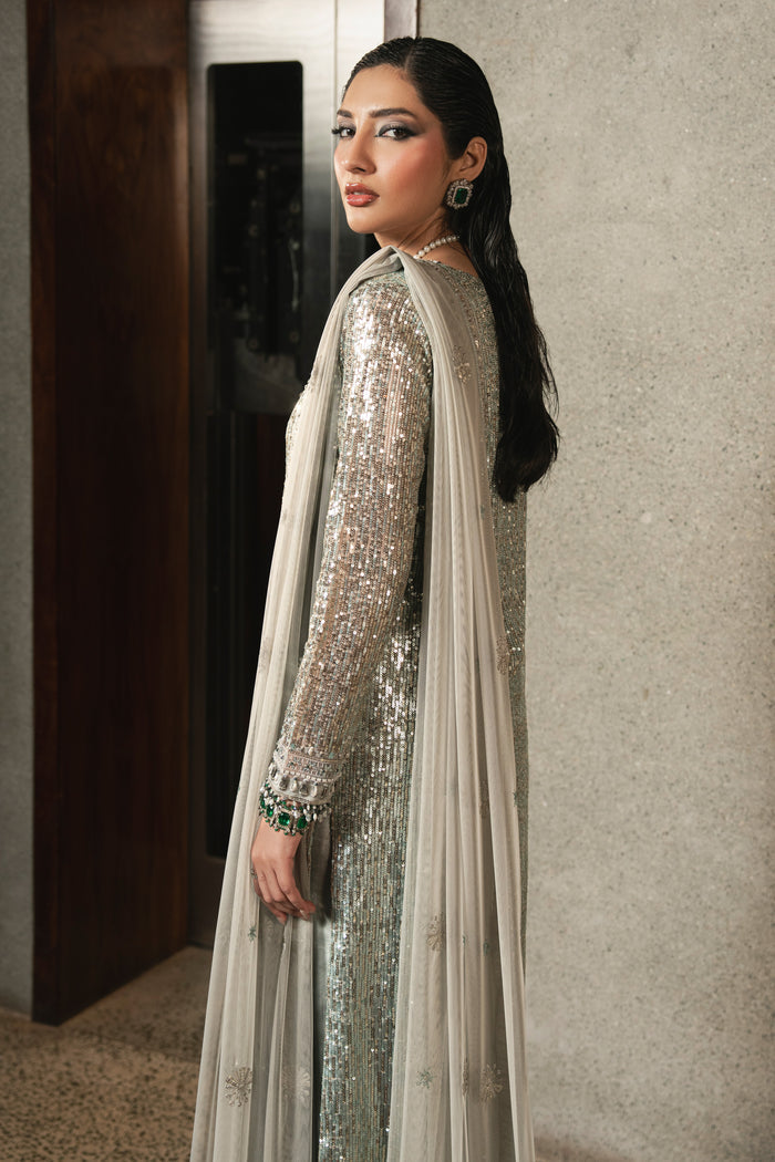 Side view of NAQSHI Urmain grey net gown highlighting elegant slit detail, adda work borders, fitted sleeves with sequins, and straight raw silk trousers.