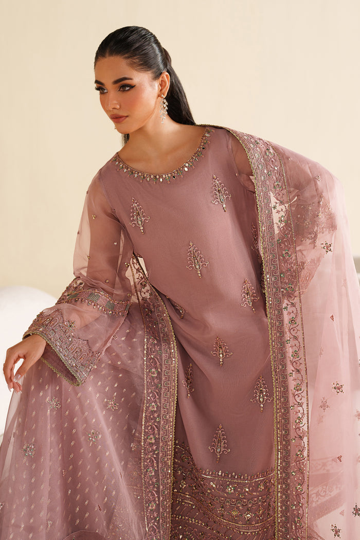 Woman wearing a pink embroidered traditional outfit with a sheer dupatta against a beige background
