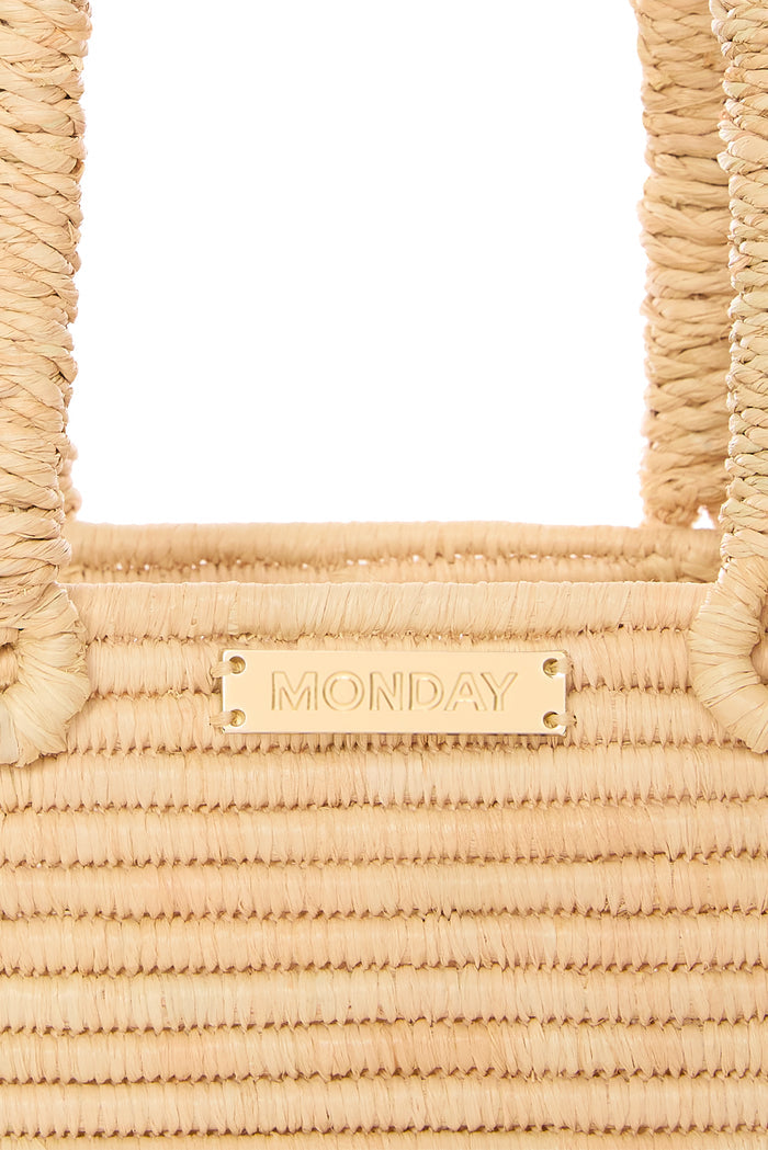 Close-up of Valencia mini woven raffia bag showing braided rope handles and gold MONDAY nameplate on a white background