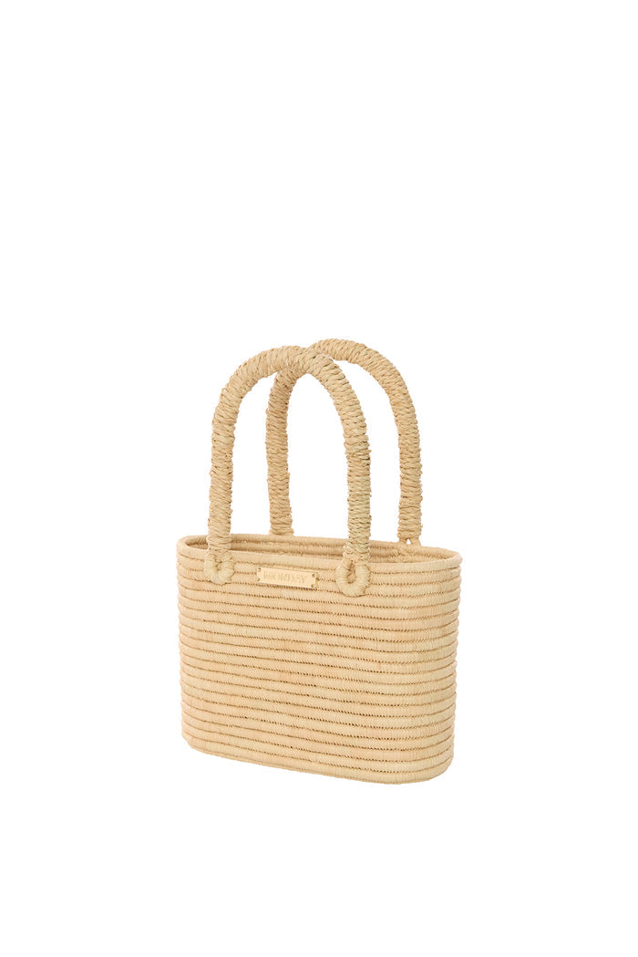Angled front view of Valencia mini woven raffia bag with rope handles and gold MONDAY nameplate on white background