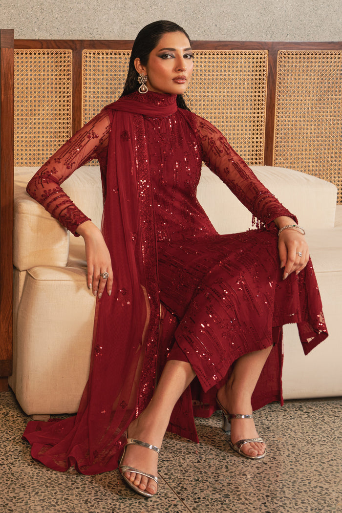 Seated view of NAQSHI Valentina rose red net 3-piece outfit highlighting straight cut trousers, flowing net dupatta, and elegant formal styling.
