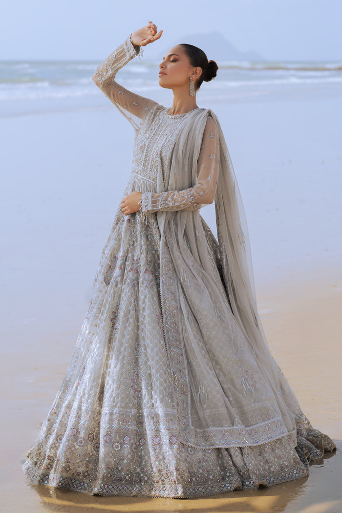 Side profile of NAQSHI Valeria showcasing the flow of silver net frock, layered sequin and floral embroidery on bodice extending to sleeves, and plain straight PK raw‑silk pants.