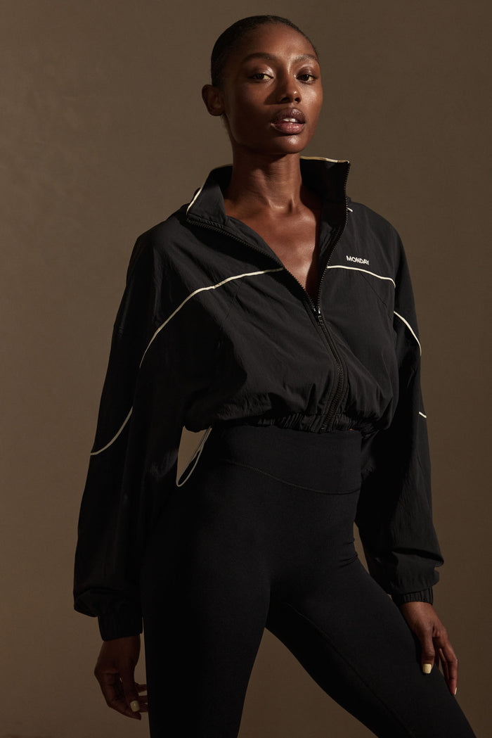 Three-quarter front of Westmount Jacket in black showing cropped zip, high collar, white piping and MONDAY logo