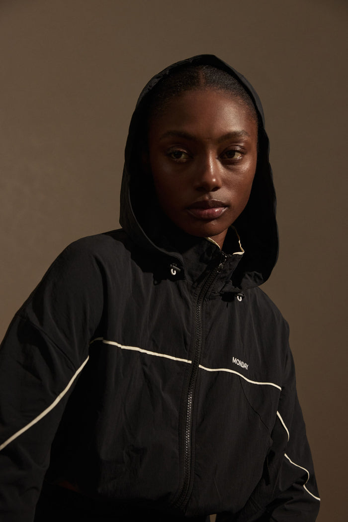 Close-up front view of Westmount Jacket in black showcasing cropped hood, white piping and MONDAY chest logo against neutral background
