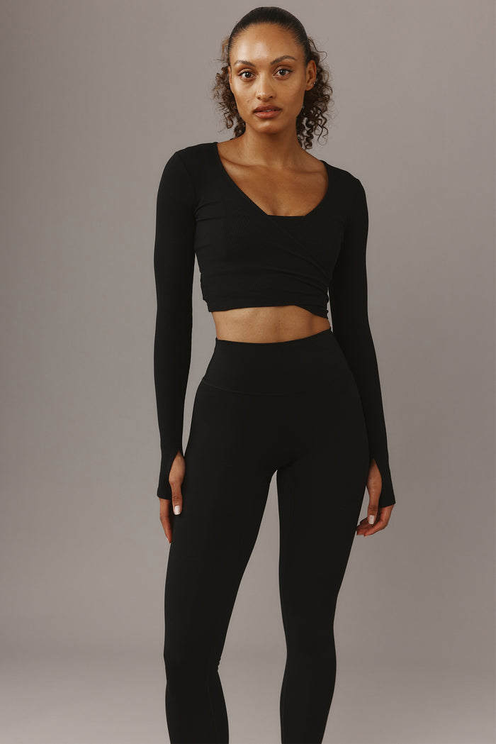 Front view of Yosemite Top in Black Rib showcasing cropped wrap front and long sleeves with thumbholes against a gray backdrop