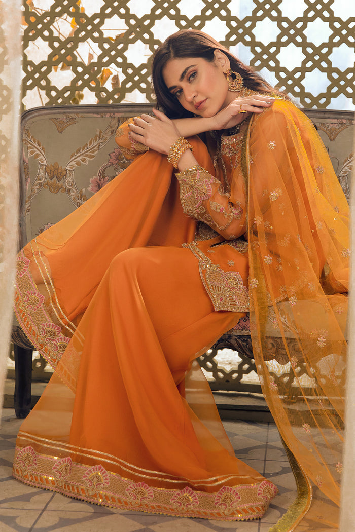 Seated pose of NAQSHI Zaryaab outfit showing rich mustard tone, short shirt design, and relaxed festive styling