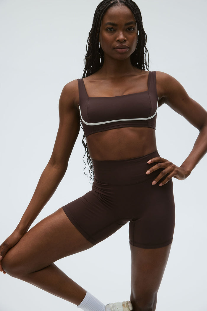 Front view of Zion Bra in espresso on model, fitted square-neck with wide straps and ivory contrast piping on light gray background