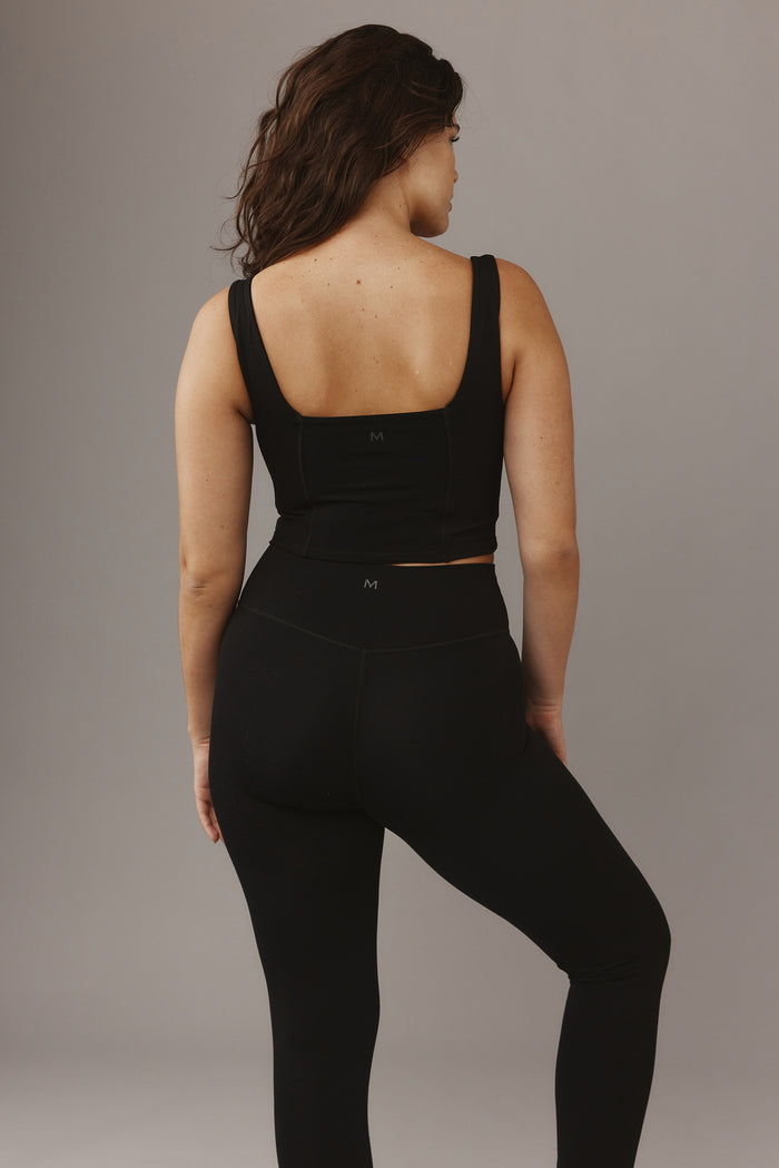 Back view of Zion Tank in black showing low square back, wide straps, cropped fit and small centered M logo on gray background